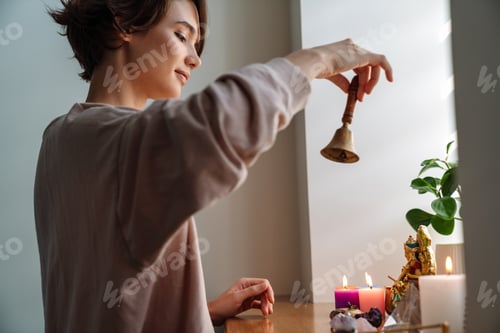 Preview: Peaceful girl ringing bell while praying at home shrine