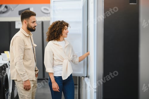 Preview: Couple choosing refrigerator in electronics store, woman opening fridge door