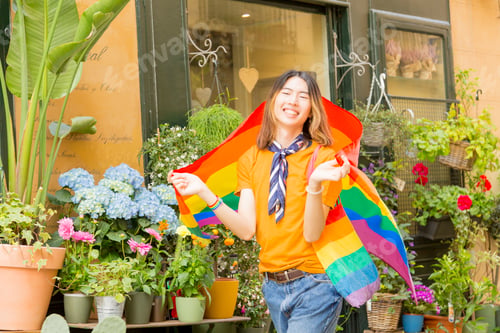 Preview: Happy young Asian celebrating Pride Day with flag in street