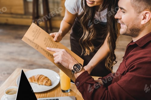 Preview: cropped view of waitress and sitting at table handsome man looking to menu in coffee house