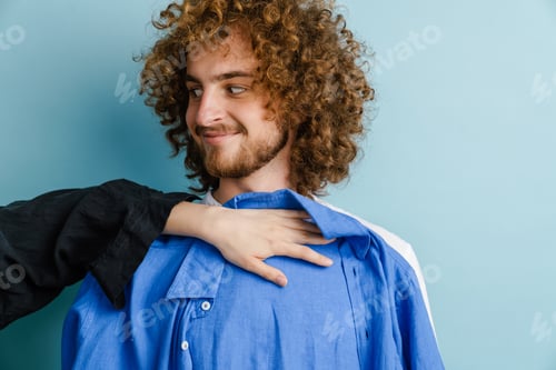 Preview: Young man with ginger curly hair smiling while trying shirt