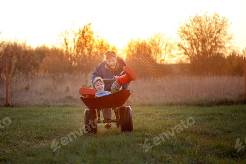 Preview: Two brothers boy ride in a wheelbarrow at sunset. Children are having fun and laughing.