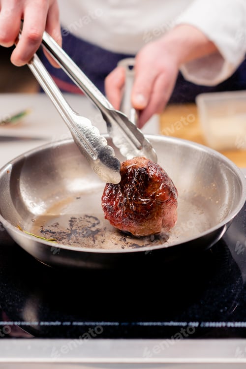 Preview: close-up in a professional kitchen with tongs holding a beef steak over hot frying pan with oil