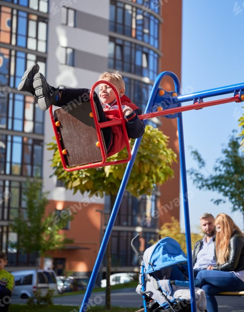 Preview: Joyful boy swinging on swing with parents behind.