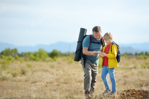 Preview: Cute schoolchild and mature father hiking together on mountain and exploring nature