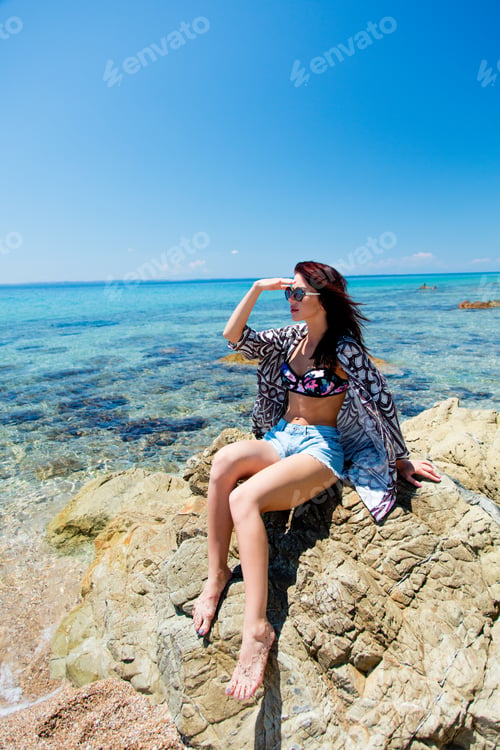 Preview: beautiful young woman sitting on big stone on the beach in Greece