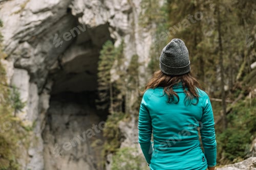 Preview: Woman being on a hike, stops to admire the huge entrance of a cave, located in Romania.