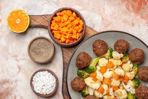 Preview: top close view broccoli and cauliflower salad and meatball on plate cutting carrot in bowl lemon