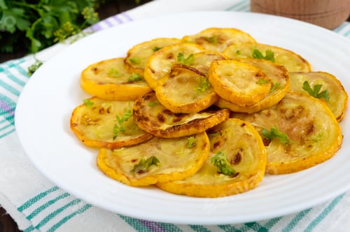 Preview: Fried zucchini slices on a white plate on a dark wooden background.