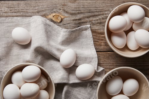Preview: top view of chicken eggs in bowls on wooden table with cloth