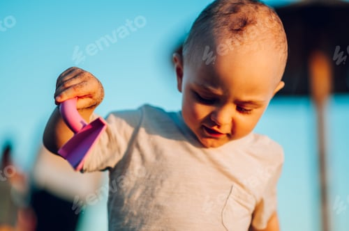 Preview: A curious little boy playing at the beach with his plastic sand shovel.