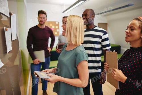 Preview: Diverse business colleagues reading paperwork together on an office wall