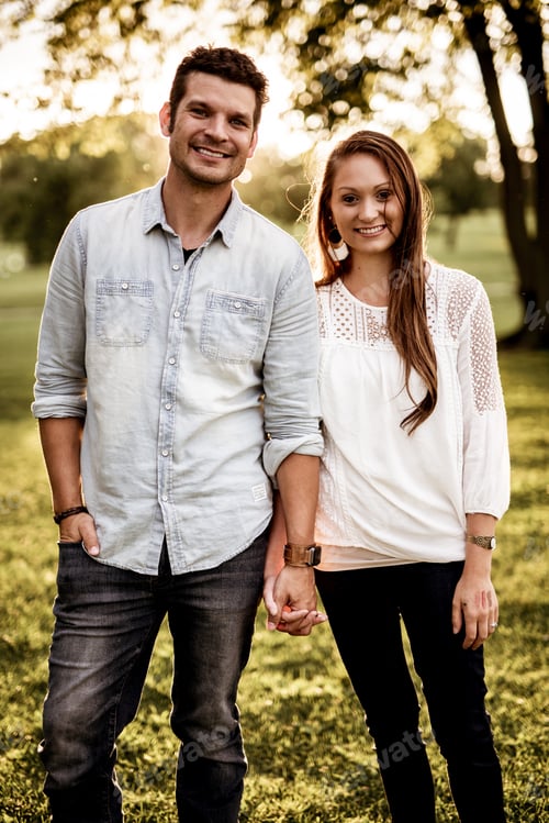Preview: Vertical shot of a happy couple holding hands and smiling at the camera with a blurred background