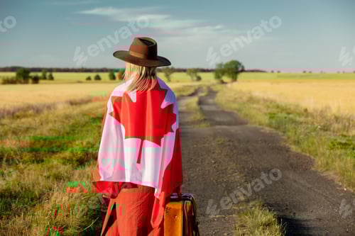 Preview: Girl in Canada flag with suitcase on country road in sunset