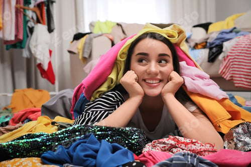 Preview: Happy young woman with lots of clothes on floor in room. Fast fashion
