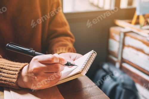 Preview: Closeup image of a woman holding and writing on blank notebook with fountain pen on wooden table