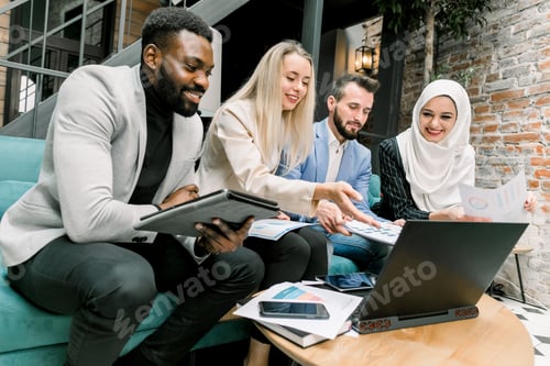 Preview: Side angle view of four young satisfied multiethnic business colleagues, smiling while looking