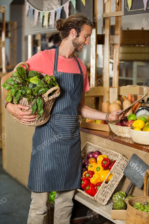 Preview: Male staff holding leafy vegetable and using digital tablet in organic section