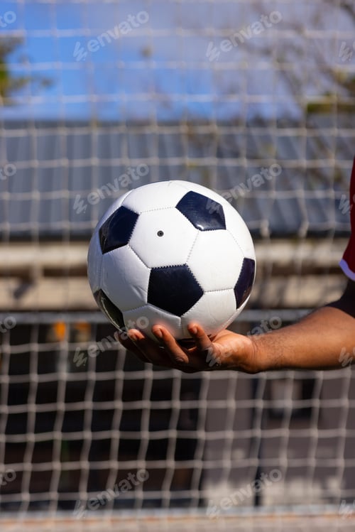 Preview: An African American young male athlete holding a soccer ball in front of a goal net on field outdoor
