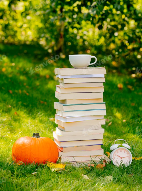 Preview: pumpkin and books with cup of coffee are on a green grass in a garden