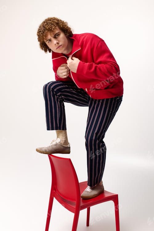 Preview: Teenager showcases bold fashion choices while playfully posing on a bright red chair