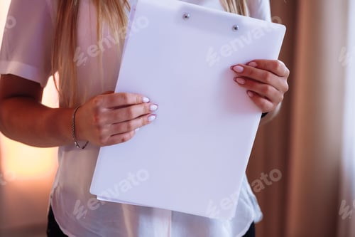 Preview: cropped photo of young woman holding a magazine or folder with mock up. girl in a white shirt