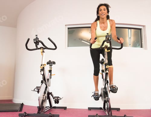 Preview: Mature woman at gym on exercise bicycle