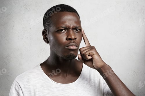 Preview: Handsome African male looking at camera with mistrust and doubt, posing against concrete wall. Thoug
