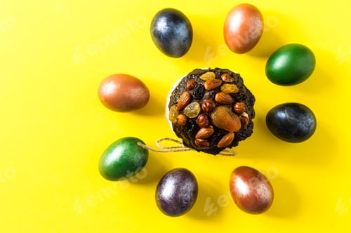 Preview: Easter cake with nuts and dried fruits on a yellow background with multi-colored colored eggs.