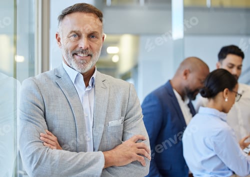 Preview: Portrait of a mature businessman standing in an office with his colleagues in the background