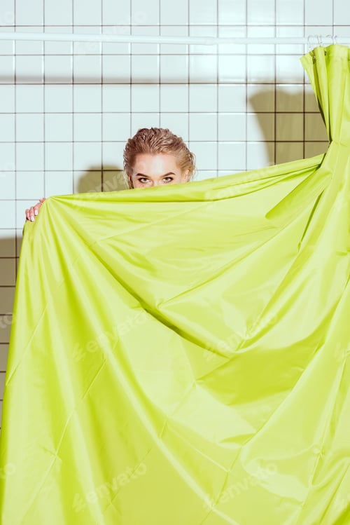 Preview: young woman hiding behind green curtain with copy space in shower