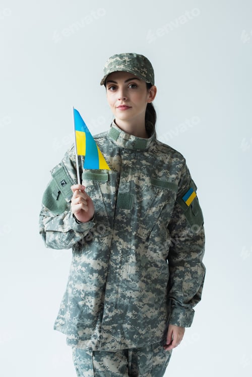 Preview: Young soldier holding ukrainian flag and looking at camera isolated on grey
