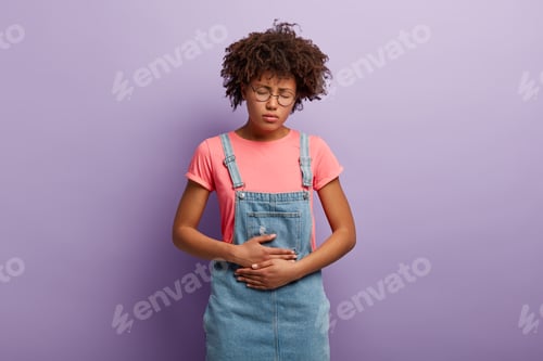 Preview: Upset woman keeps hands on belly, suffers from menstruation pain, cramps and stomachache, has chroni