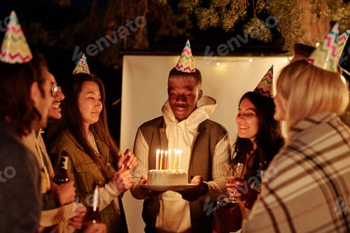 Preview: Young African man looking at candles on birthday cake while making wish