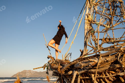 Preview: Young woman with upped leg on decorative wooden ship near water on shore