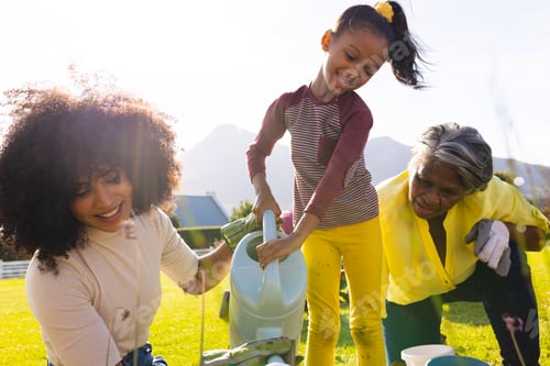 Preview: Multiracial happy girl with mother and grandmother watering plants against clear sky in yard