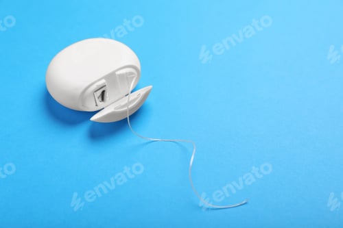 Preview: Container with dental floss on light blue background, closeup. Space for text