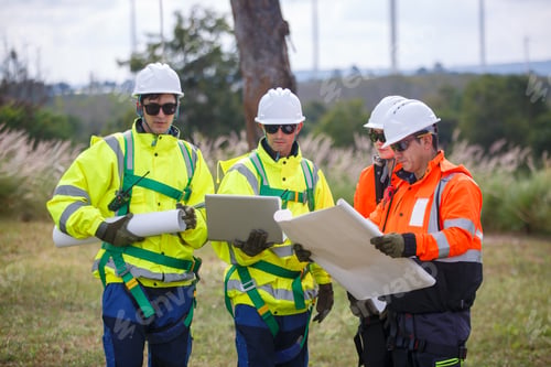Preview: Workers review plans for a construction project in a field on a sunny day