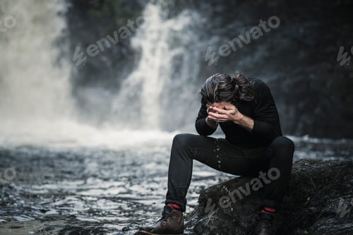 Preview: A man sitting washing his face in a mountain stream by a waterfall.