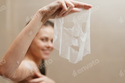 Preview: Smiling woman holding a facial sheet mask, preparing for a skincare routine. Relaxation and self