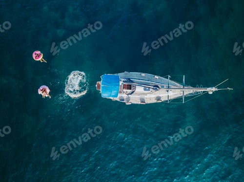 Preview: Aerial view of individuals enjoying a leisurely swim next to a moored boat in clear blue waters