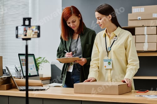 Preview: Young volunteer with packed parcel standing by her colleague with document