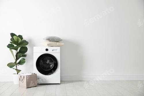 Preview: Washing machine, clean laundry and houseplant near white wall indoors. Space for text