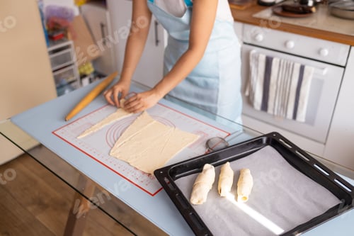 Preview: Producing classic croissants at home. Woman is rolling dough into rolls for further baking. French p