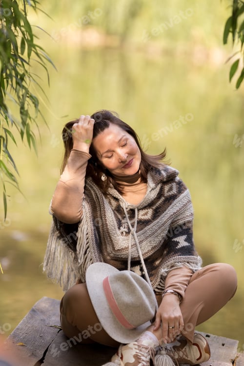 Preview: fashionable beautiful woman sitting on the bridge on the lake in autumn