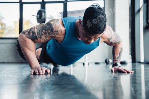 Preview: focused young sportsman doing plank exercise at gym