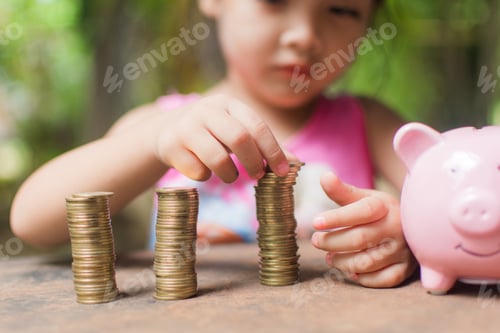 Preview: cute little girl holding coin of money and put in pink piggy bank with blur background.