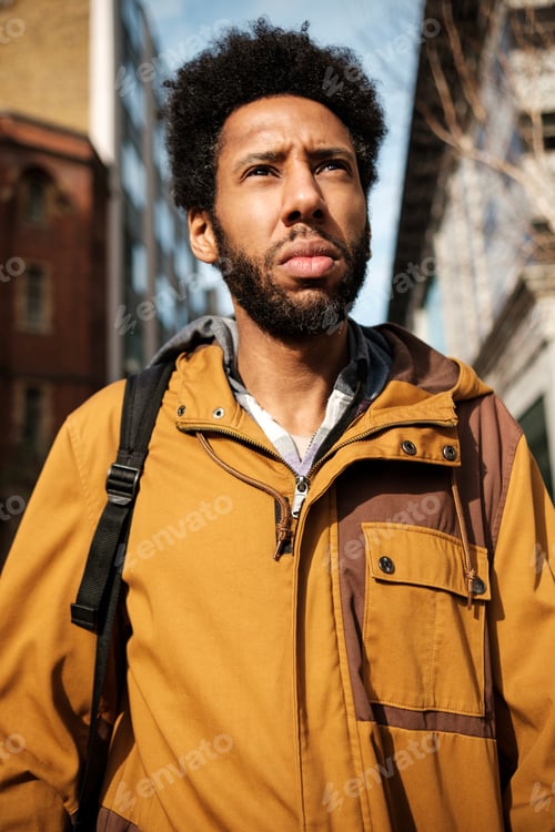 Preview: Young man looking up wearing casual clothes and backpack in the city