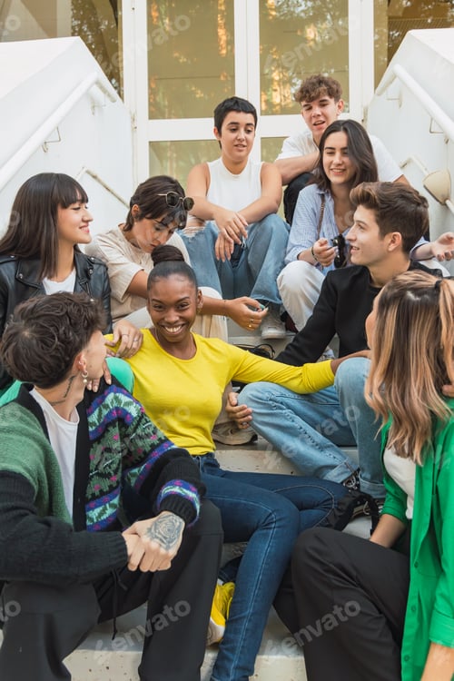 Preview: Group of happy diverse friends sitting on stairs of glass door entrance in daylight