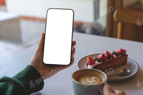 Preview: A woman holding mobile phone with blank screen while drinking coffee and eating dessert in cafe